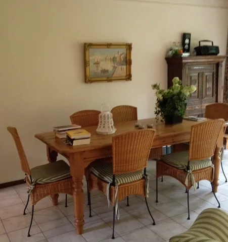 De eettafel met rieten stoelen, onder een schilderij van een haven.