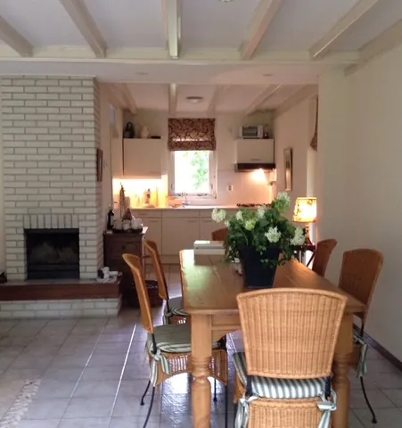 Vanaf de open haard gezien: de lange houten eettafel met rieten stoelen en achterin de keuken.